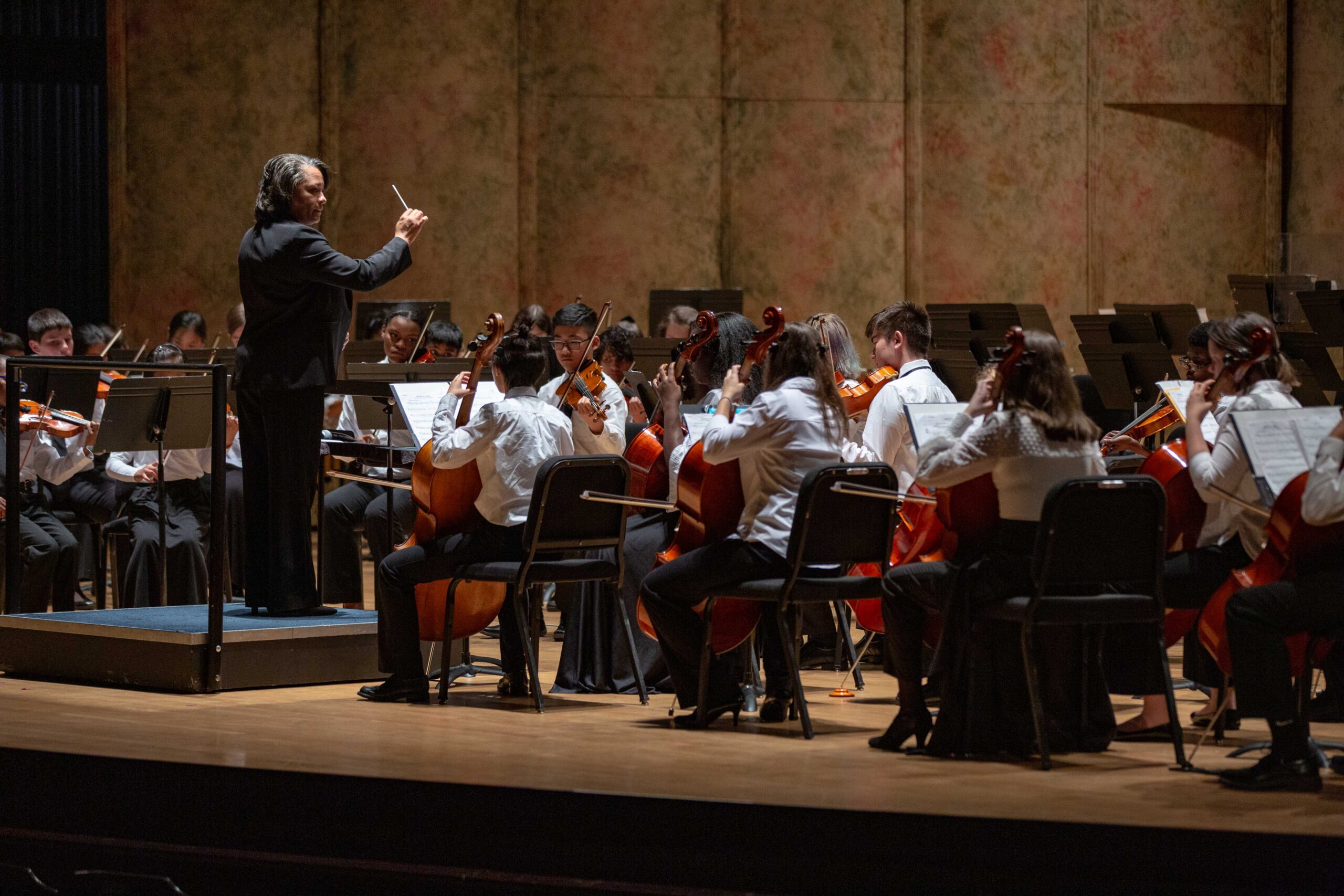 Christie-Jo Adams conducts violinists, violists, cellists, and double bassists, all dressed in concert black and white, on stage at the Carpenter Theatre.
