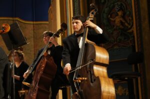 Double bassists play their instruments on stage at the Carpenter Theatre. At the forefront is Harry Grossman, wearing a tuxedo.