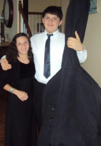 Two middle-school students stand side by side. The one on the left is dressed in all black. The one on the right, Harry, wears a white button-down with a tie, and is holding his double bass in its case.